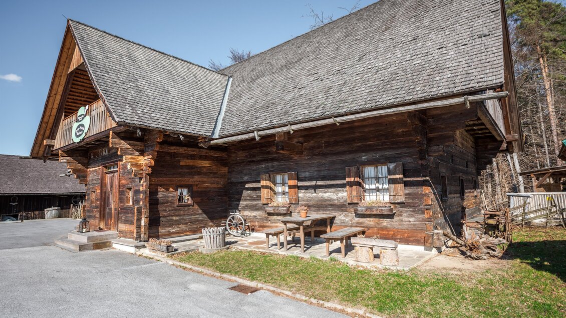 Kern Buam Museum in einem historischen Holzbau mit Schindeldach, kleinen Fenstern und Sitzbänken vor dem Gebäude in Voitsberg | © DieAbbilderei