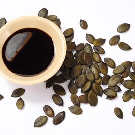 Ein kleiner Schüssel mit dunklem Öl liegt in der Mitte, umgeben von Kürbiskernen. Die Zutaten bieten eine gesunde und schmackhafte Kombination. | © AdobeStock_151549464.jpeg