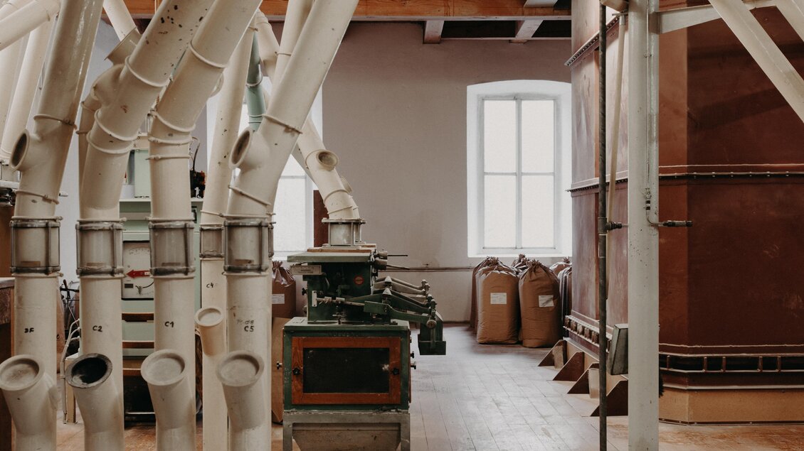Eine historische Mühle mit Rohren und Maschinen. Im Hintergrund sind Säcke mit Mehl zu sehen. | © RM SW GmbH | webquartier.at