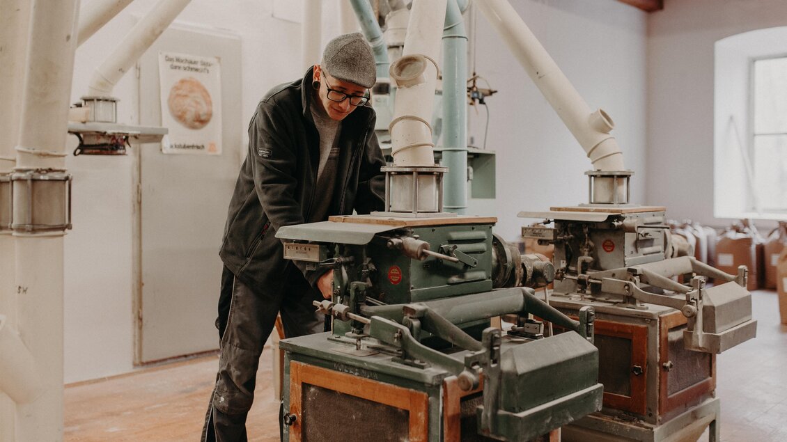 Ein Mann arbeitet an alten Mühlen in einer hellen, industriellen Umgebung. Im Hintergrund sind einige Maschinen und saubere Wände zu sehen. | © RM SW GmbH | webquartier.at