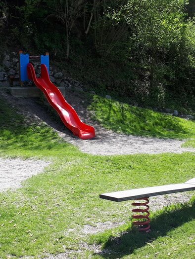<p>Der Spielplatz im Kurpark in Bad Aussee mit einer roten Rutsche, einer Wippe und Schaukel. Der Bereich ist von grünem Gras und Bäumen umgeben.</p> | © Stadtgemeinde Bad Aussee/Ziermayer