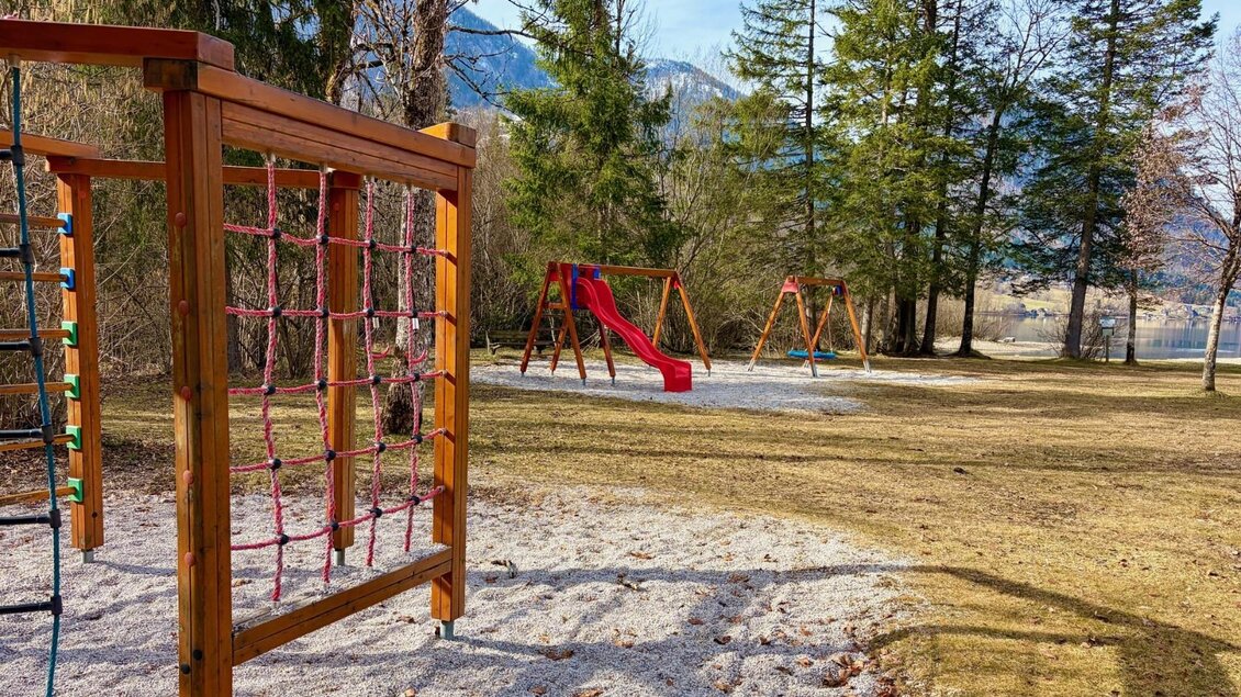 Ein Spielplatz mit einem Klettergerüst und einer Rutsche steht in einer grünen Wiese. Im Hintergrund sind Bäume und Berge zu sehen. | © TVB Ausseerland