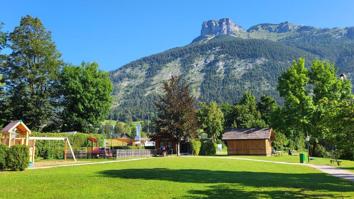 Eine grüne Wiese mit Spielplatz und Bäumen, umgeben von Bergen. Der Himmel ist klar und blau. | © Petra Kirchschlager