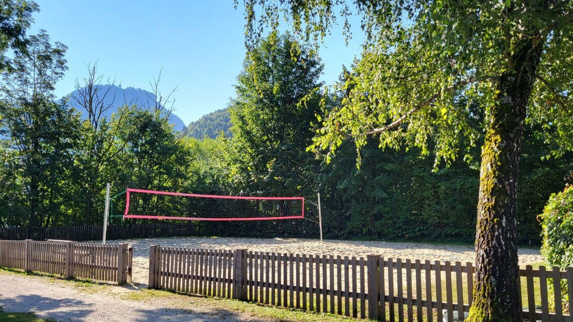 Ein Volleyballplatz in der Natur, umgeben von Bäumen und Bergen. Das Spielfeld ist mit einem roten Netz markiert. | © Petra Kirchschlager