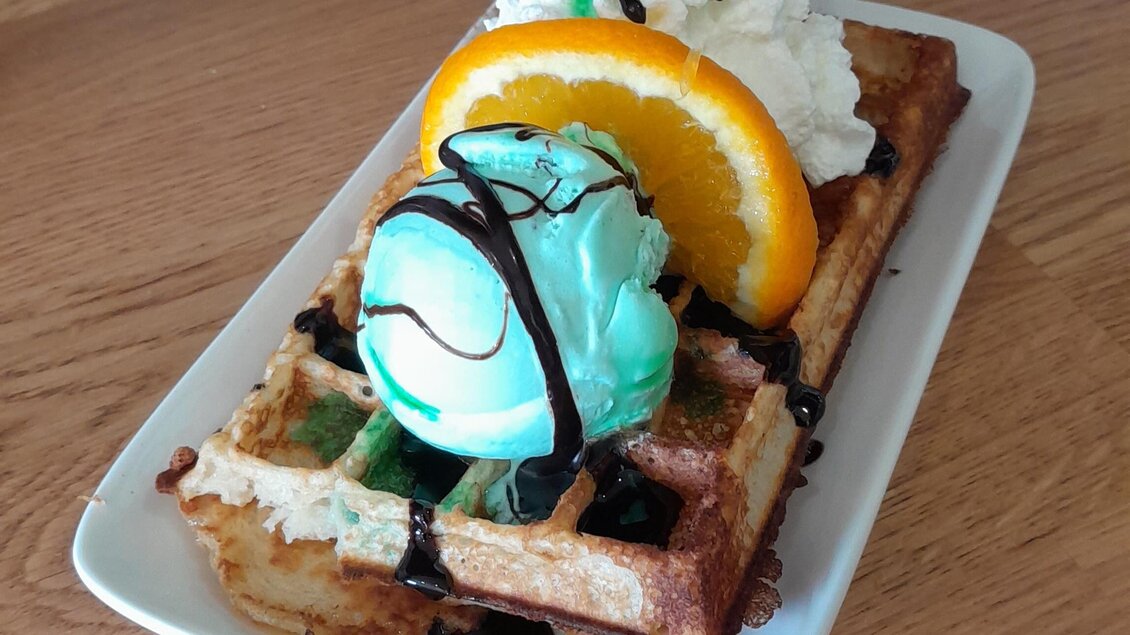 Ein leckeres Waffelgericht mit zwei Kugeln Eis, Sahne und einer Orangenscheibe. Es ist auf einem weißen Teller angerichtet und sieht verführerisch aus. | © Mountain Adventure Golf