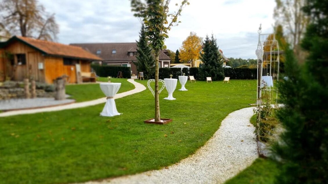Ein schöner Garten mit grünem Rasen und geschwungenen Wegen. Es gibt verschiedene Dekorationen und Tische für eine Veranstaltung im Freien. | © Gasthaus Draxler