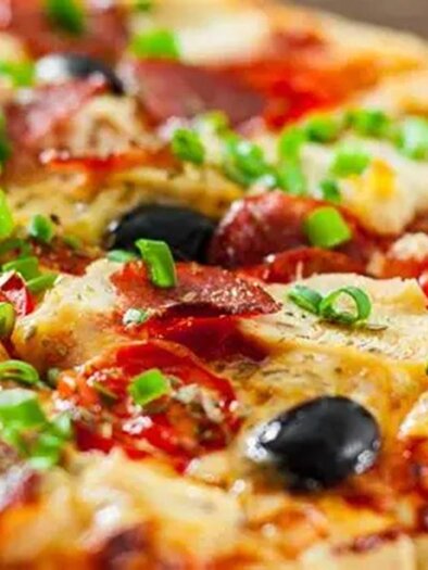 Eine leckere Pizza mit Salami, Oliven und frischen Frühlingszwiebeln. Der geschmolzene Käse und die bunten Zutaten machen sie appetitlich. | © Kirchenwirt Pizzeria