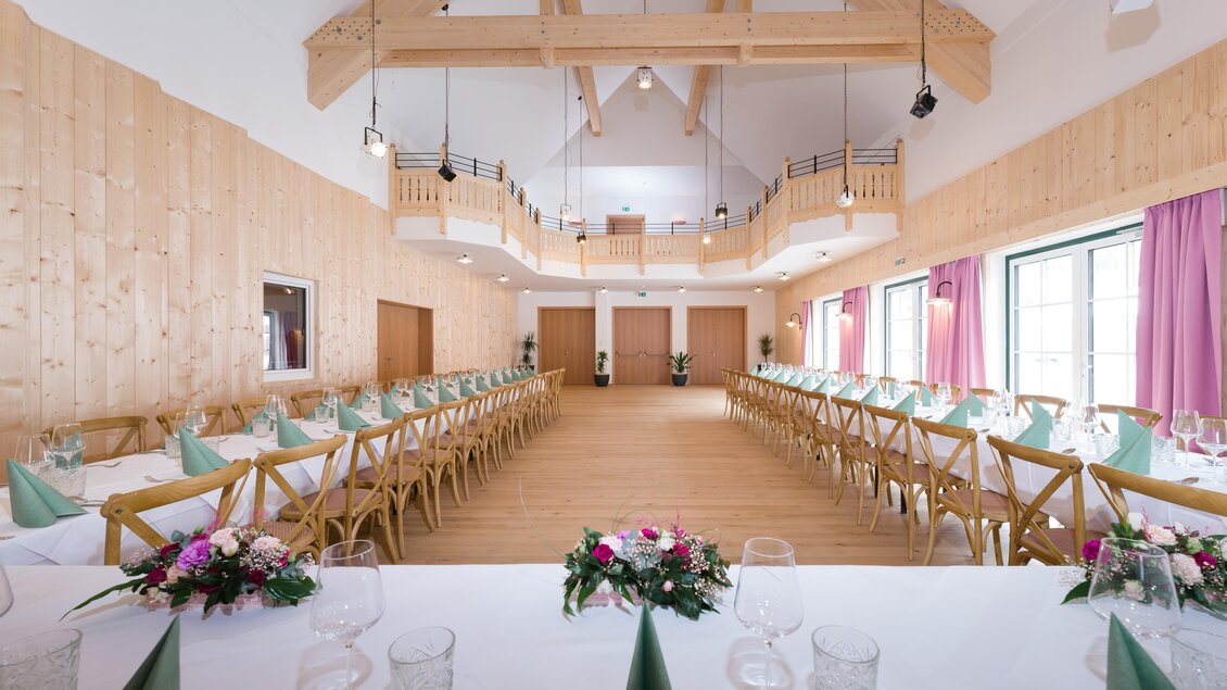 Ein eleganter Veranstaltungsraum mit Holzwänden und großen Fenstern. Tische sind für eine Feier gedeckt und eine festliche Atmosphäre ist zu spüren. | © www.zloam.at