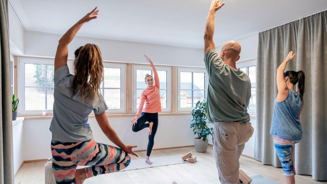 Eine Gruppe von vier Personen macht Yoga in einem hellen Raum. Sie stehen in verschiedenen Posen und strahlen Entspannung aus. | © www.zloam.at