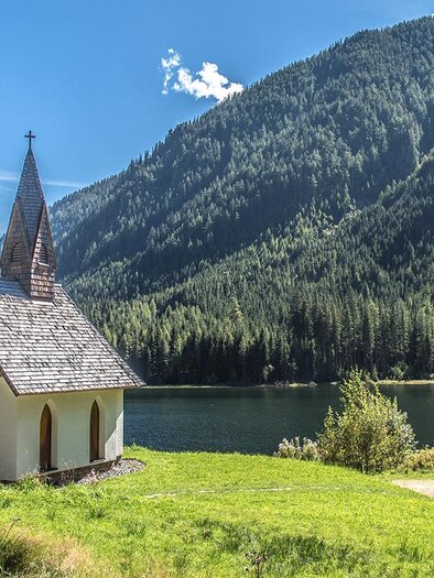 Eine kleine, idyllische Kapelle am Ufer eines klaren Sees, umgeben von hohen Bergen und dichten Wäldern. Der Himmel ist blau und strahlend. | © Erlebnisregion Murtal