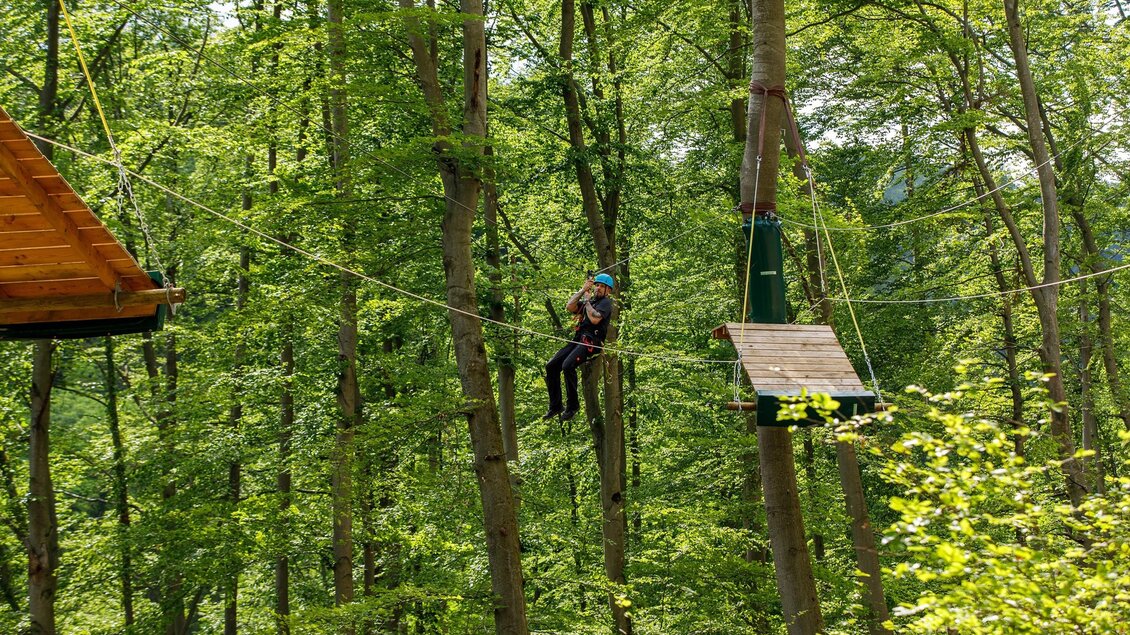 Person im Kletterpark Piber gleitet gesichert zwischen Plattformen im Waldseilgarten. | © Kletterpark Piber Eddy Aldrian