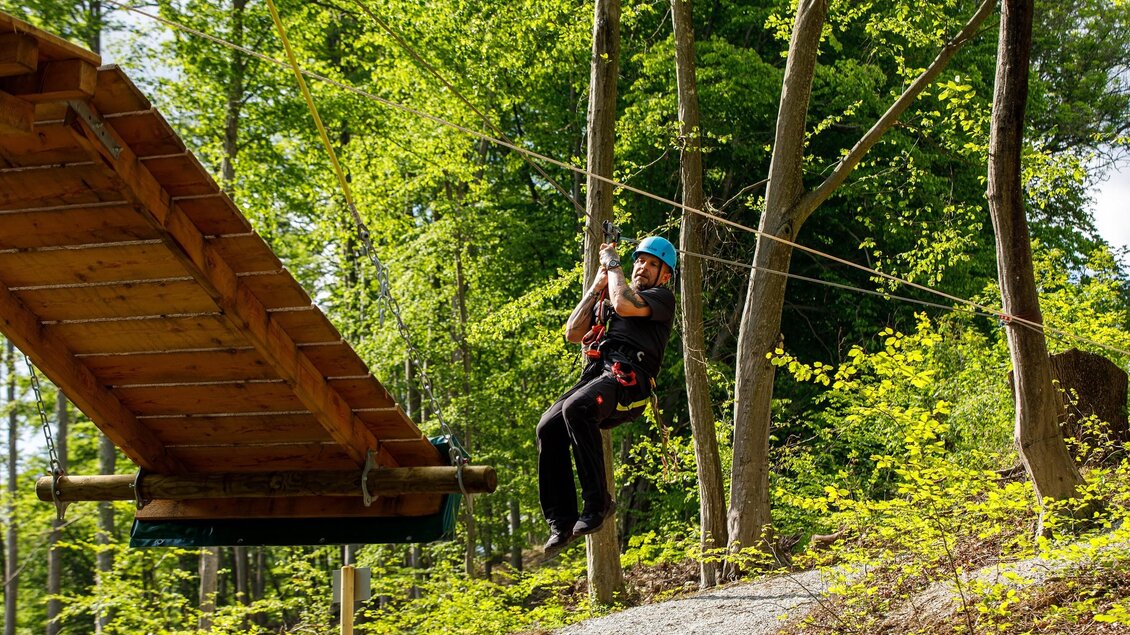 Person im Kletterpark Piber fährt gesichert auf Seilrutsche zwischen Bäumen im Wald. | © Kletterpark Piber Eddy Aldrian