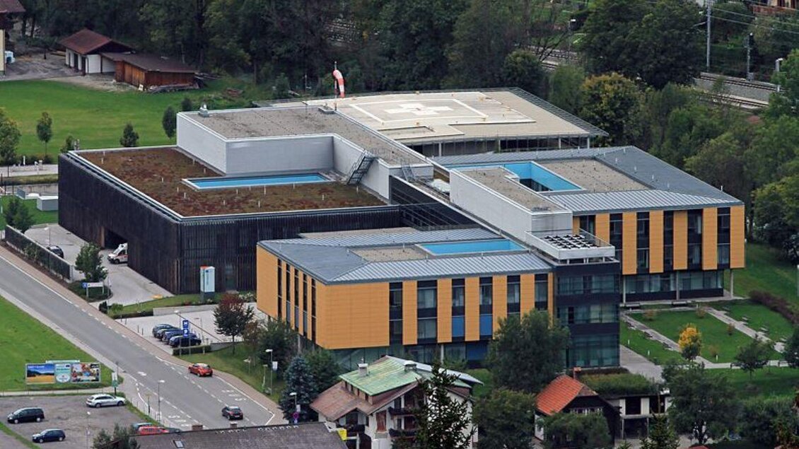 Ein modernes Gebäude mit großen Fenstern und gelben Akzenten. Die Umgebung ist gepflegt mit grünen Rasenflächen und Bäumen. | © Klinik Diakonissen Schladming