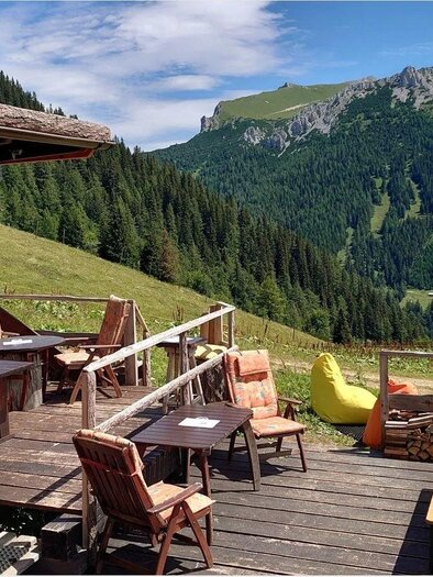 Eine gemütliche Terrasse mit Holzmöbeln und Blick auf die Berge. Im Hintergrund erstrecken sich grüne Wälder und eine klare Himmel. | © Hirner