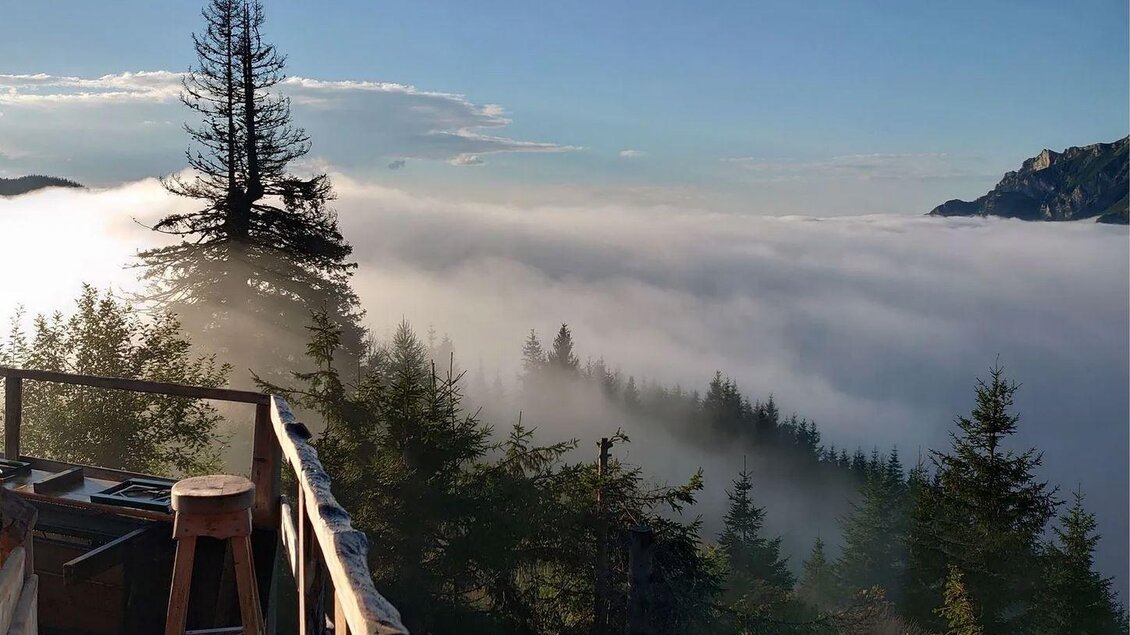 Eine atemberaubende Aussicht von einer Holzplattform über Nebel und Wälder. Die Sonnenstrahlen beleuchten die Landschaft und schaffen eine friedliche Atmosphäre. | © Hirner