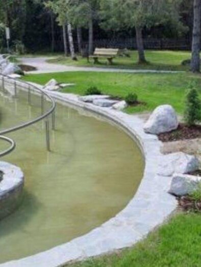 A quiet park with a clear water feature and green grass. There are stones and seating areas for visitors. | © Marktgemeinde Gröbming