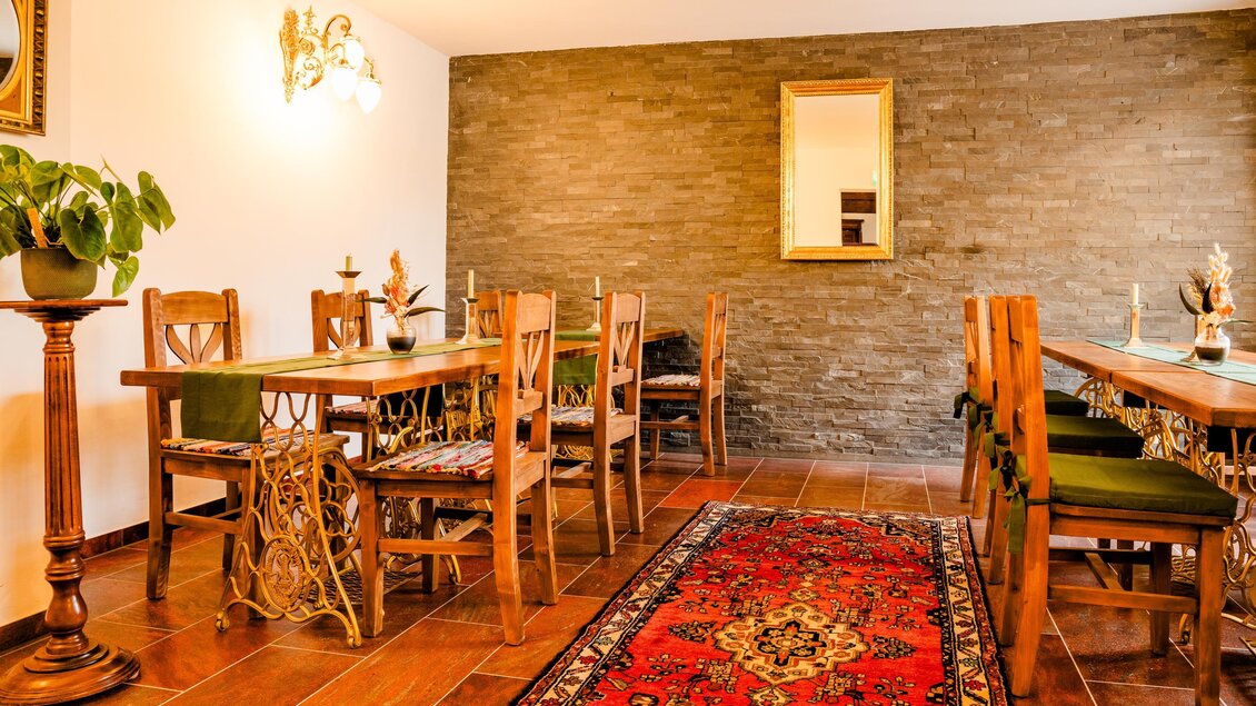 Gastraum der Konoba Sidro in Sankt Bartholomä mit Holztischen, Stühlen, Teppich und Steinwand. | © Region Graz - Mias Photoart-7