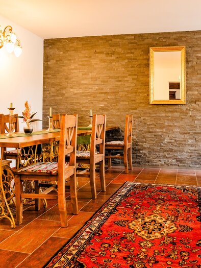 Gastraum der Konoba Sidro in Sankt Bartholomä mit Holztischen, Stühlen, Teppich und Steinwand. | © Region Graz - Mias Photoart-7