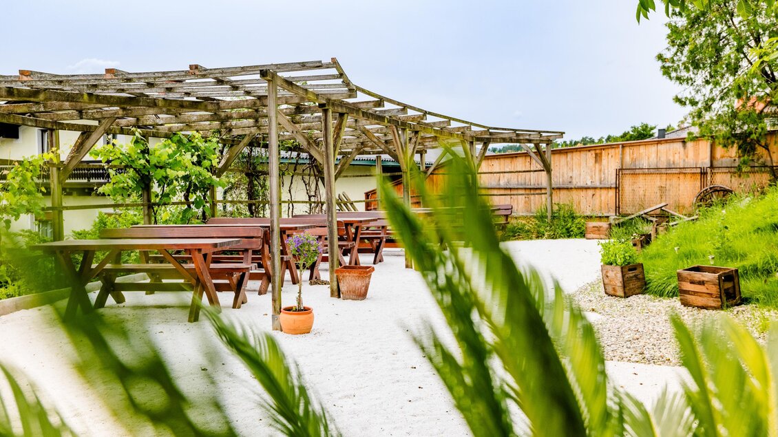 Begrünter Gastgarten der Konoba Sidro in Sankt Bartholomä mit Holzpergola, Sitzplätzen und Kiesfläche. | © Region Graz - Mias Photoart