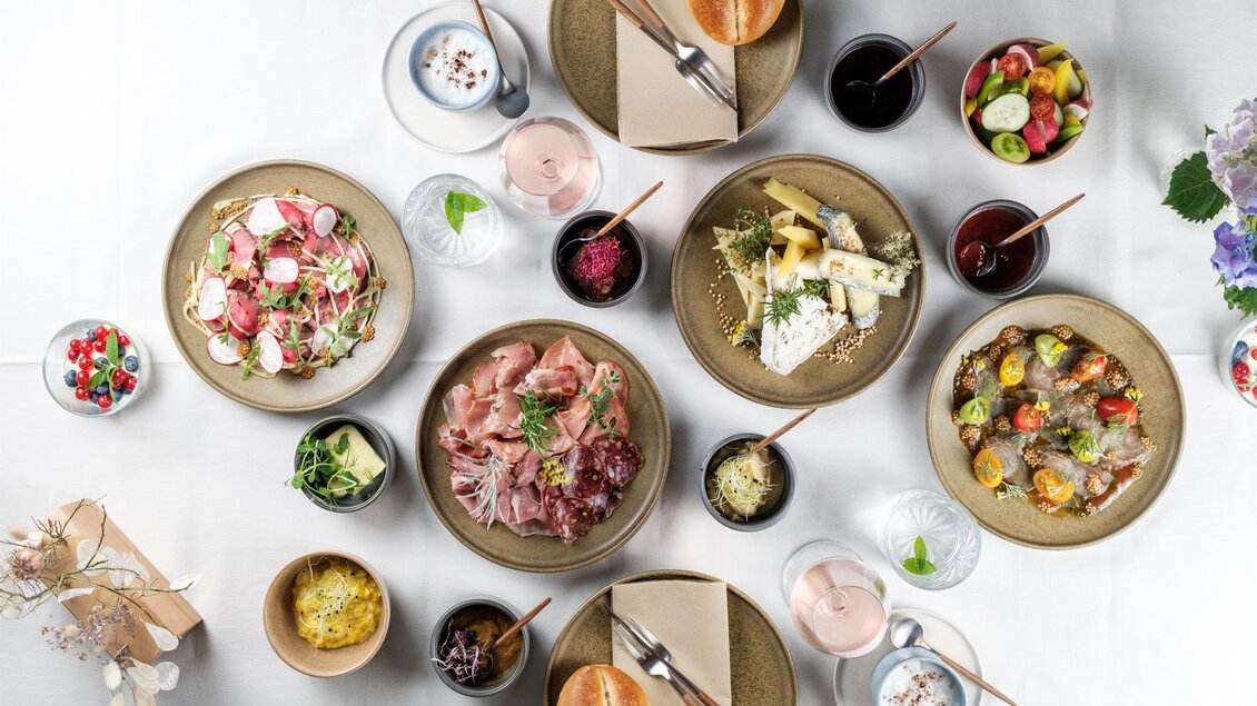 Ein schön gedeckter Tisch mit verschiedenen Gerichten. Es gibt Salate, Fleisch, Gemüse und Desserts in ansprechenden Schalen und Tellern. | © Kostbar, Thomas Gartner