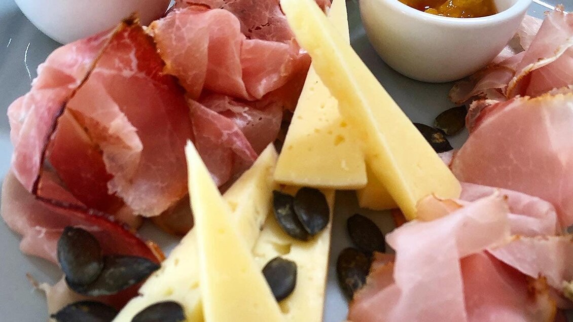 Ein Teller mit verschiedenen Wurstsorten, Käsestücken und Kürbiskernen. Dazu zwei kleine Schalen mit Senf und einer süßen Soße. | © KostBar Café & Greißlerei