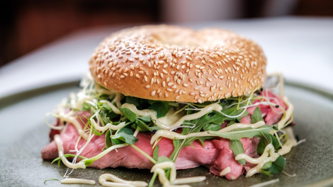 Ein Sesambrötchen gefüllt mit zartem Fleisch, frischem Salat und Sprossen. Das Gericht sieht lecker und einladend aus. | © Kostbar, Thomas Gartner