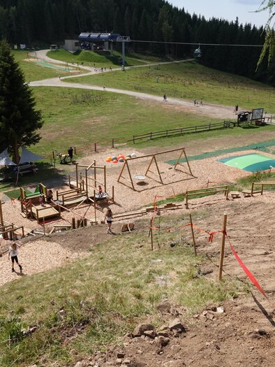 Ein Spielplatz in einer bergigen Umgebung mit Schaukeln und einem grünen Spielbereich. Im Hintergrund sind Wanderwege und Bäume sichtbar. | © Grebenzen Höhen