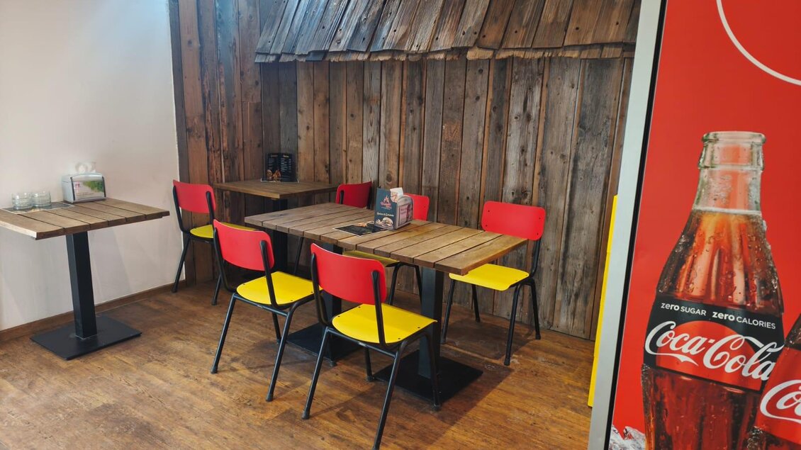 Ein gemütlicher Restaurantbereich mit Tisch und bunten Stühlen. Die Wände sind aus Holz und es gibt eine Coca-Cola-Werbung im Hintergrund. | © TVB Murau