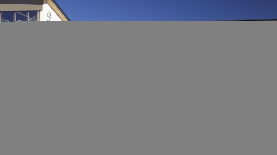Ein modernes Gebäude mit großen Glasfenstern und einem Eingangsbereich. Die Fassaden sind schlicht und ansprechend gestaltet. | © Krug Sports- & Health Center Ramsau