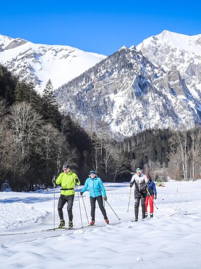 Eine Gruppe von Skifahrern bewegt sich durch eine verschneite Landschaft. Im Hintergrund sind majestätische Berge unter blauem Himmel zu sehen. | © Foto Freisinger