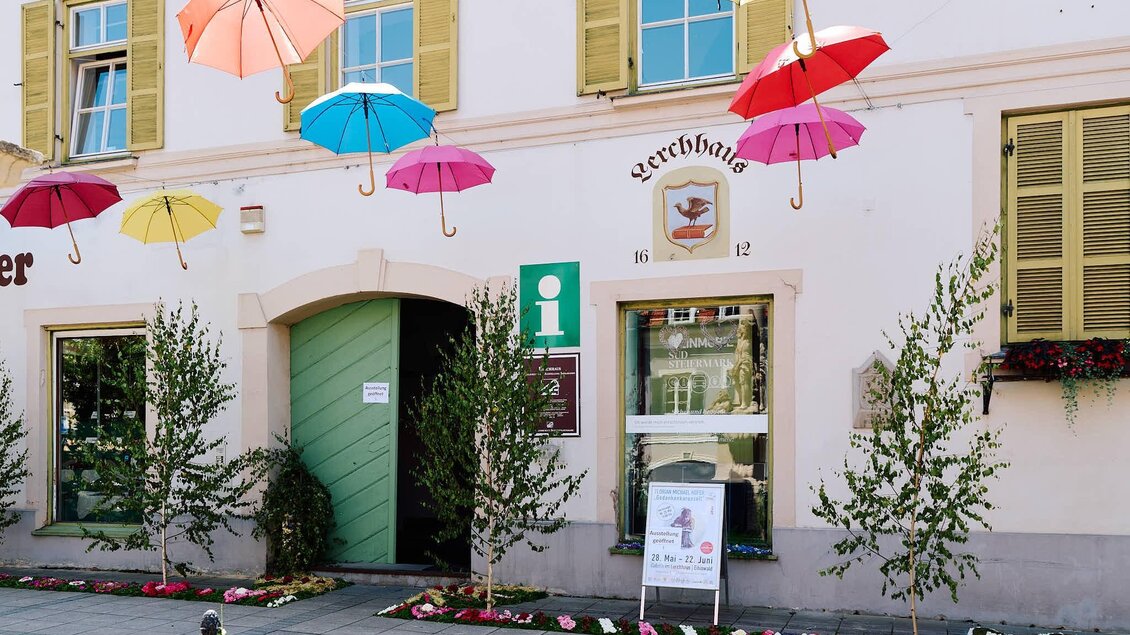 Ein bunt dekoriertes Gebäude mit Schirmen, die über dem Eingang hängen. Vor dem Gebäude stehen kleine Bäume und ein Informationsschild. | © Kultur- & Museumsverein Eibiswald