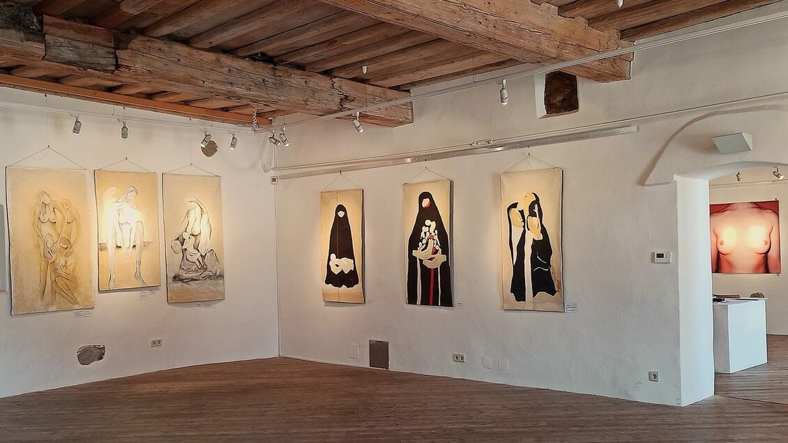 Ein heller Ausstellungsraum mit verschiedenen Gemälden an den Wänden. Die Bilder zeigen Menschen in unterschiedlichen Stilen und Farben. | © Kultur- & Museumsverein Eibiswald