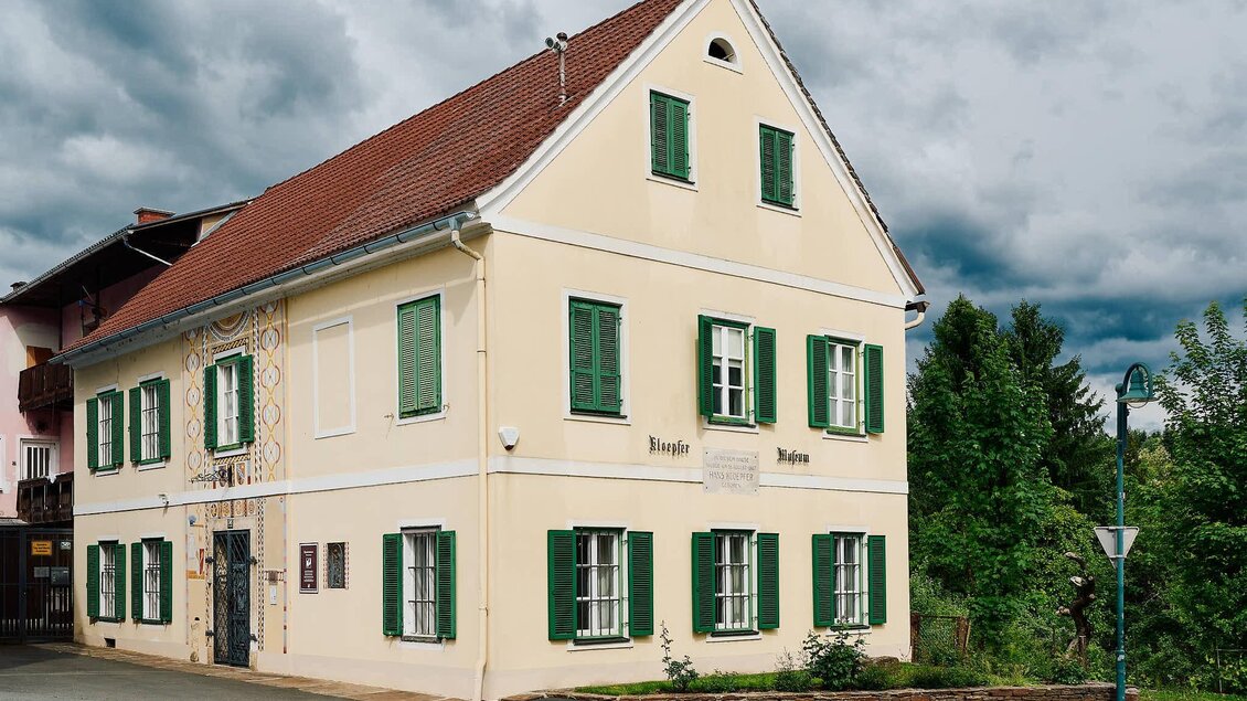 Ein schönes, gelbes Gebäude mit grünen Fenstern und einem roten Dach. Im Hintergrund sind Bäume und ein grauer Himmel zu sehen. | © Kultur- & Museumsverein Eibiswald