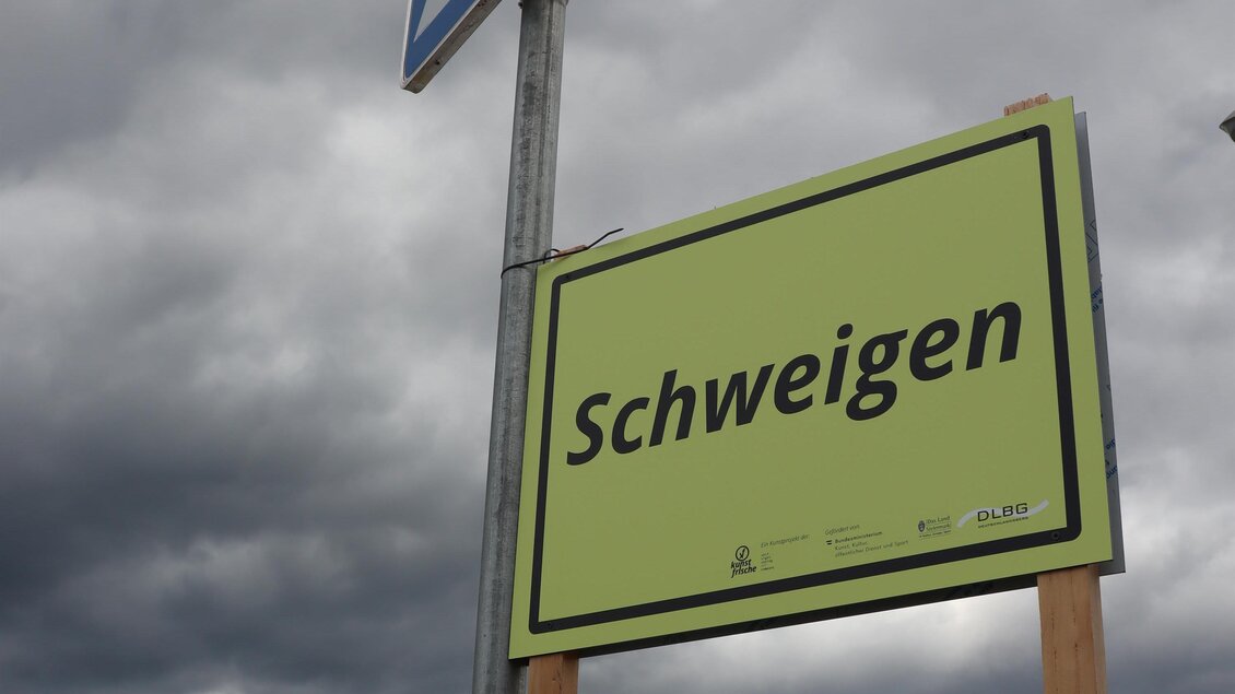 Ein Verkehrsschild zeigt an, dass Schweigen gefordert ist. Im Hintergrund sind graue, bewölkte Himmel zu sehen. | © itshe+io