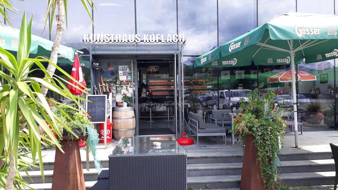 Eingang des Kunst & Kultur Café in Köflach mit Sitzbereich, Pflanzen, Sonnenschirmen und Blick ins Café in der Steiermark.  | © TV Lipizzanerheimat