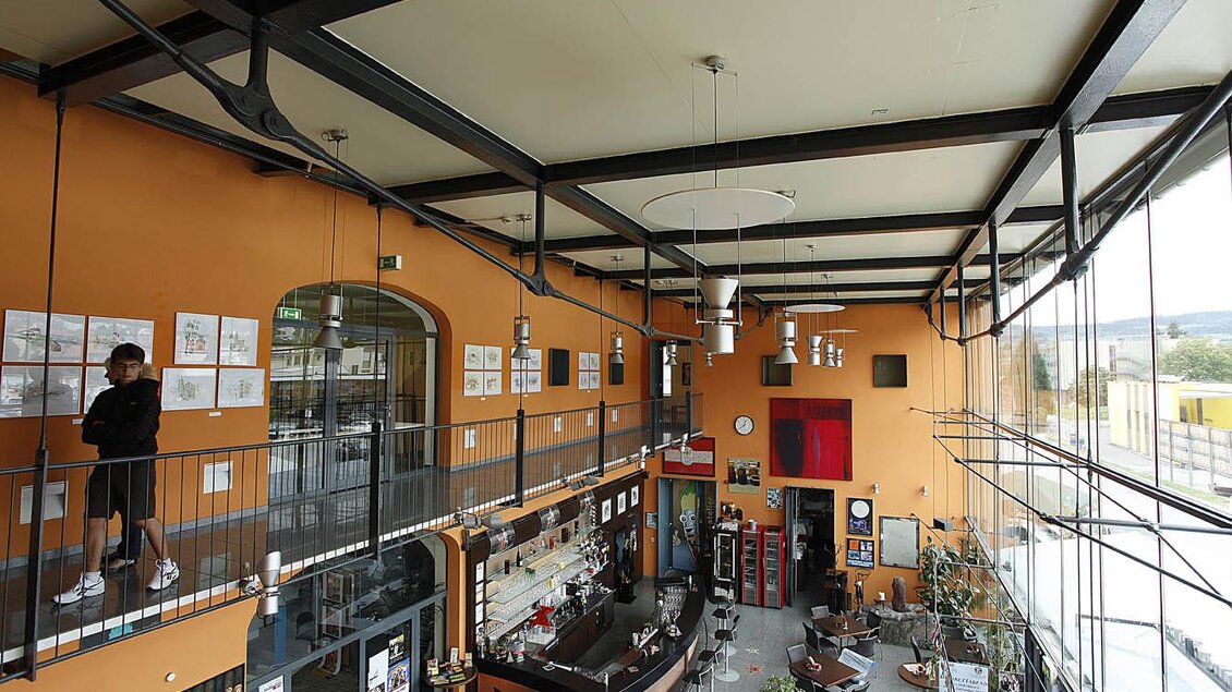 Moderner Innenraum im Kunst & Kultur Café in Köflach mit Galerieebene, Bar, Sitzbereichen und großen Fensterfronten. | © Enrico Caracciolo