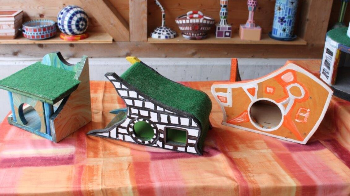 Drei kreative und bunte Katzenhäuser stehen auf einem Tisch. Die Häuser haben verschiedene Formen und Farben, mit Kunstrasen auf den Dächern.