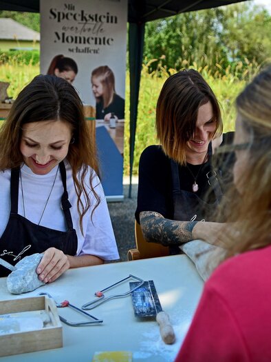 Three women are working at a table, creating stones. They are smiling and seem to be enjoying the activity. | © Strassegger