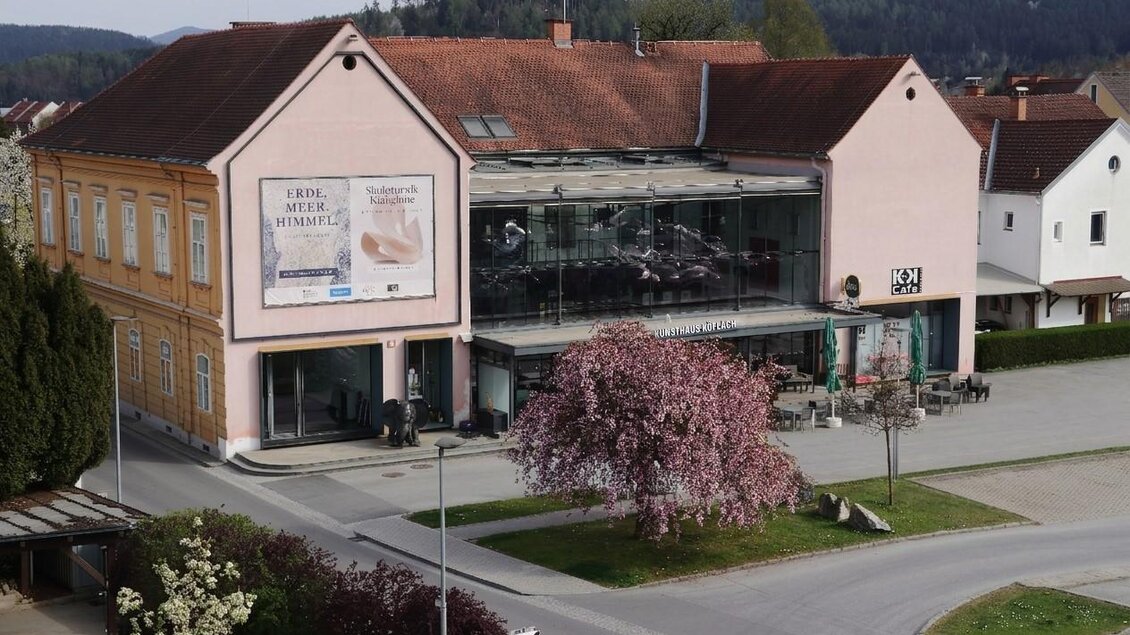 Ansicht des Kunsthaus Köflach mit Glasfassade, Café und blühendem Baum im Ortszentrum der Steiermark.  | © Kunsthaus Köflach
