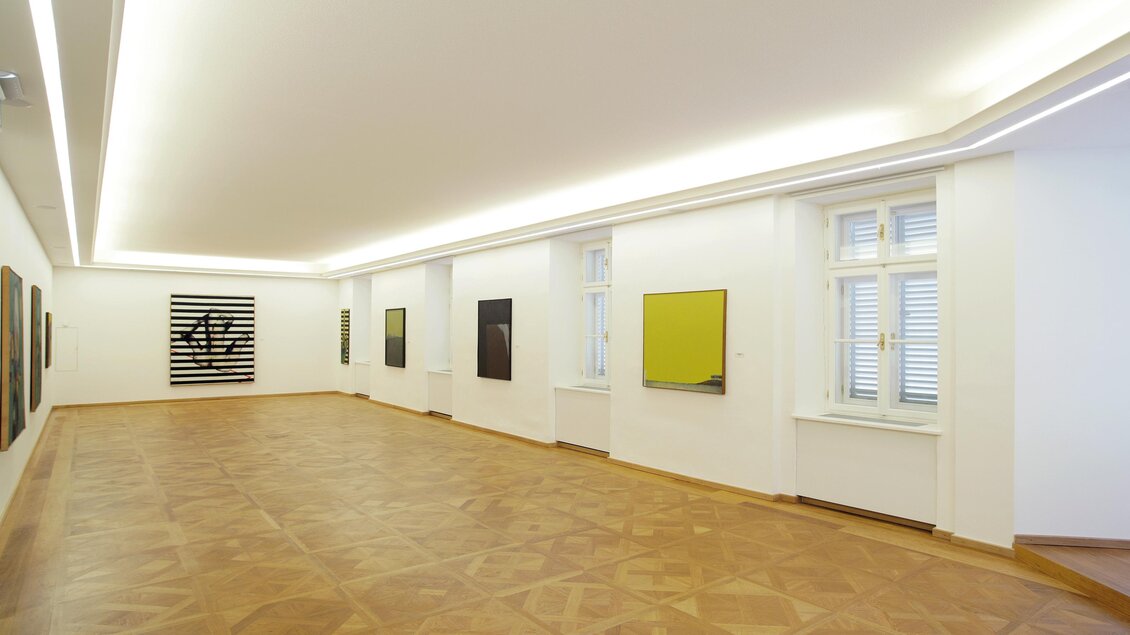 Ein heller, moderner Ausstellungsraum mit mehreren Kunstwerken an den Wänden. Der Boden ist aus Holz und die Beleuchtung ist gleichmäßig. | © Kunsthaus Weiz