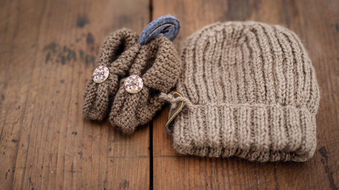 Braune Haube und gestricktes Accessoire aus Alpakawolle auf Holztisch am Bio Schusterbauernhof in Geisttal-Södingberg. | © Die Abbilderei