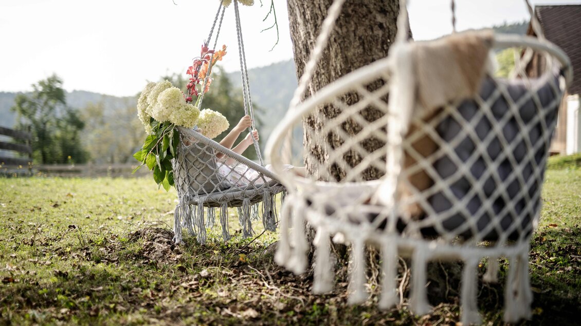 <p>Zwei Hängesessel mit Blumen unter einem Baum am Bio Schusterbauerhof in Geisttal-Södingberg. </p> | © Die Abbilderei