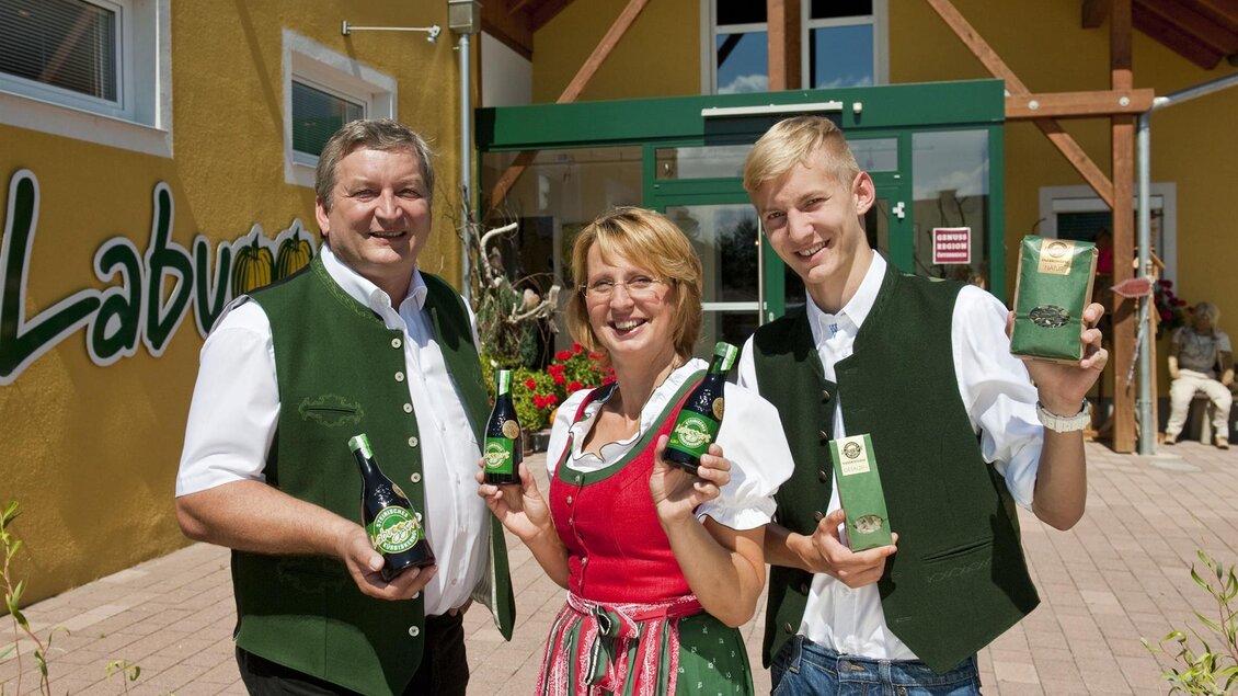 Eine Gruppe von Personen steht vor einem Geschäft. Sie halten Flaschen und Produkte in der Hand und tragen traditionelle Kleidung. | © Labugger´s Kernölpresse