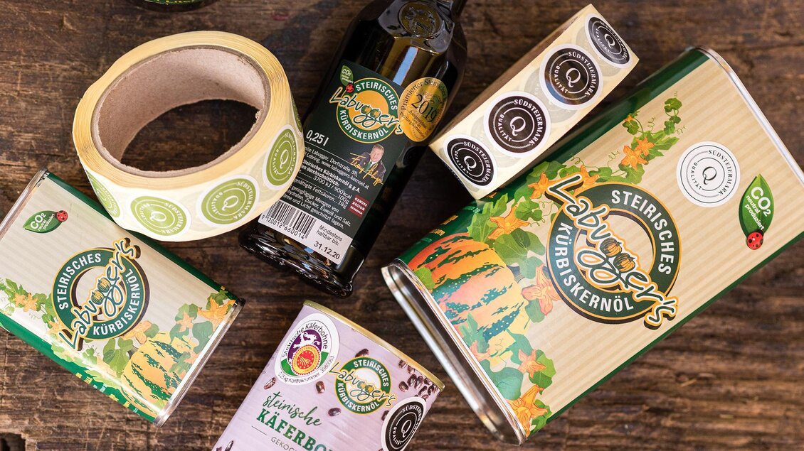 Eine Auswahl an Produkten mit Kürbiskernöl und Etiketten auf einem Holztisch. Die Verpackungen sind bunt gestaltet und zeigen verschiedene Sorten des Öls. | © RM SWS GmbH | webquartier.at