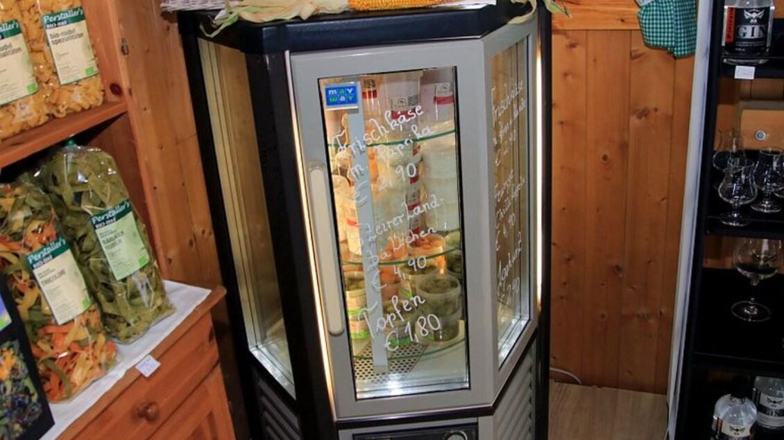 Ein Kühlschrank steht in einem Holzraum. Er zeigt verschiedene Produkte und hat eine klare Glastür. | © Karl Mayer