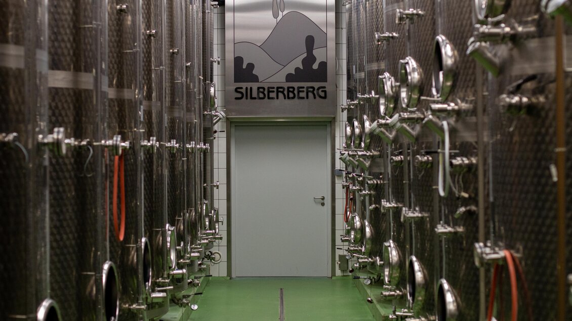 Ein moderner Weinkeller mit metallenen Lagertanks. An der Wand hängt ein Schild mit der Aufschrift "Silberberg". | © @Silberberg