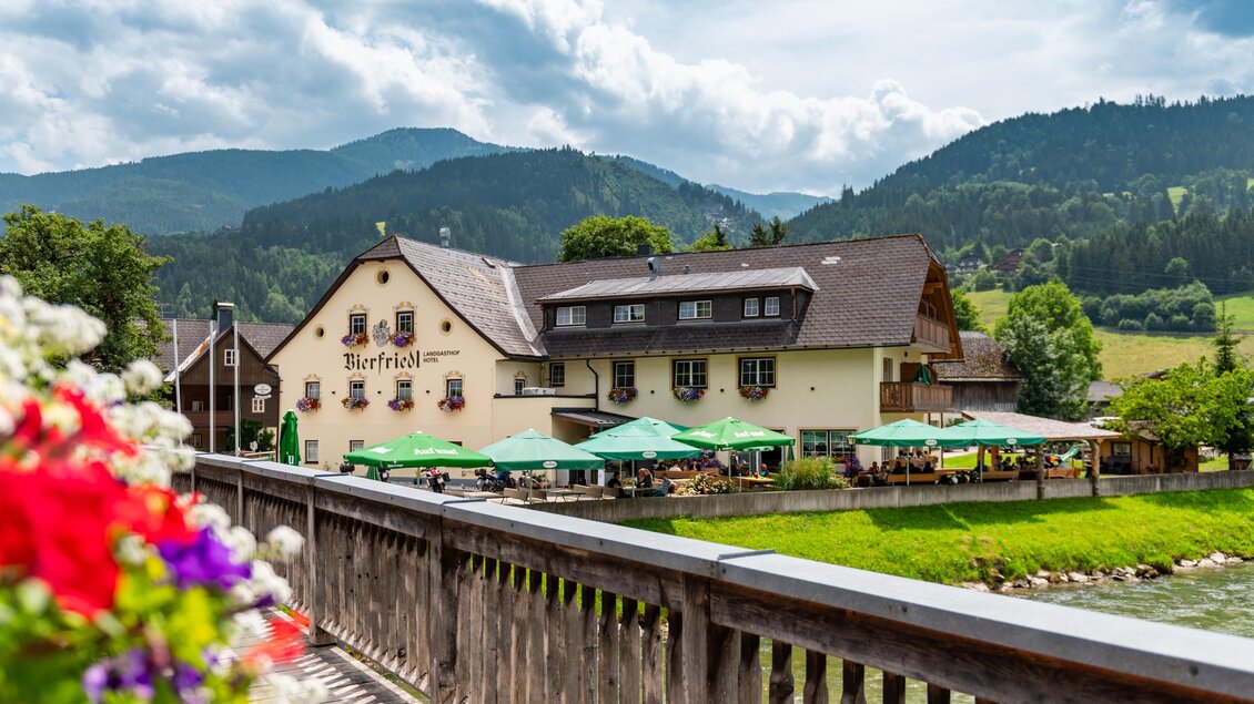 Ein gemütliches Gasthaus mit blühenden Blumen und einem schönen Ausblick auf den Fluss. Die umliegende Natur und die Terrasse laden zum Verweilen ein. | © Landgasthof Bierfriedl