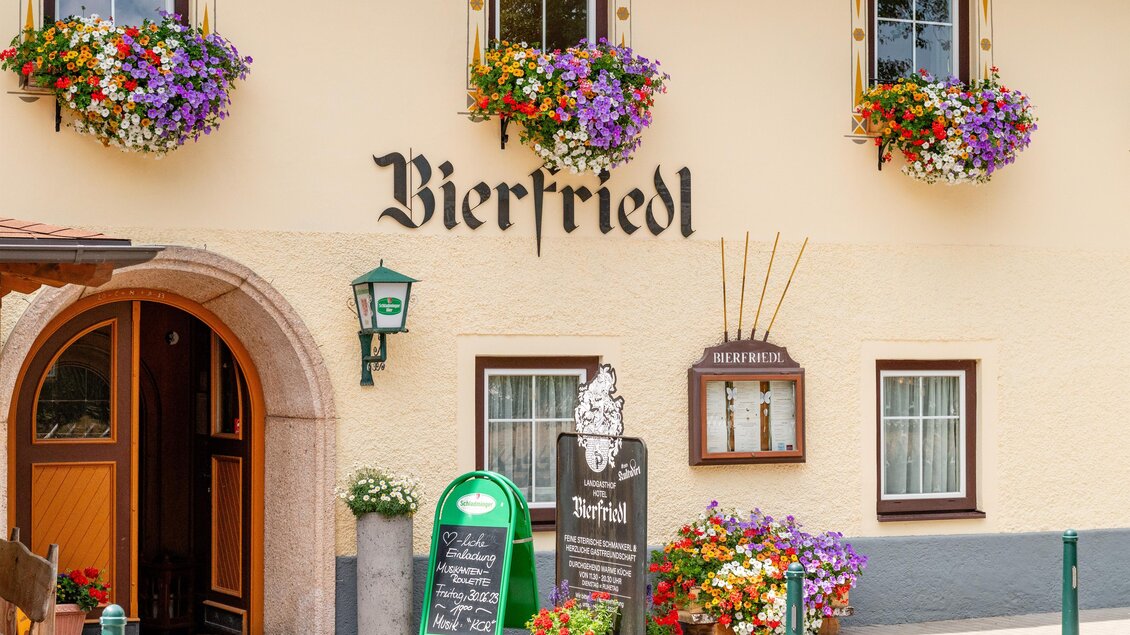 Ein gemütliches Gasthaus mit dem Namen "Bierfriedl". Die Fassade ist mit bunten Blumen dekoriert und es gibt eine einladende Eingangstür.