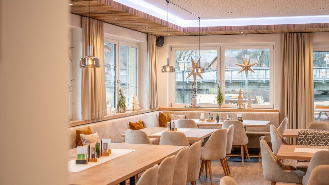 Ein modern gestaltetes Restaurant mit hellen Sitzplätzen und warmen Holzdetails. Große Fenster bieten einen Blick nach draußen und schaffen eine einladende Atmosphäre.