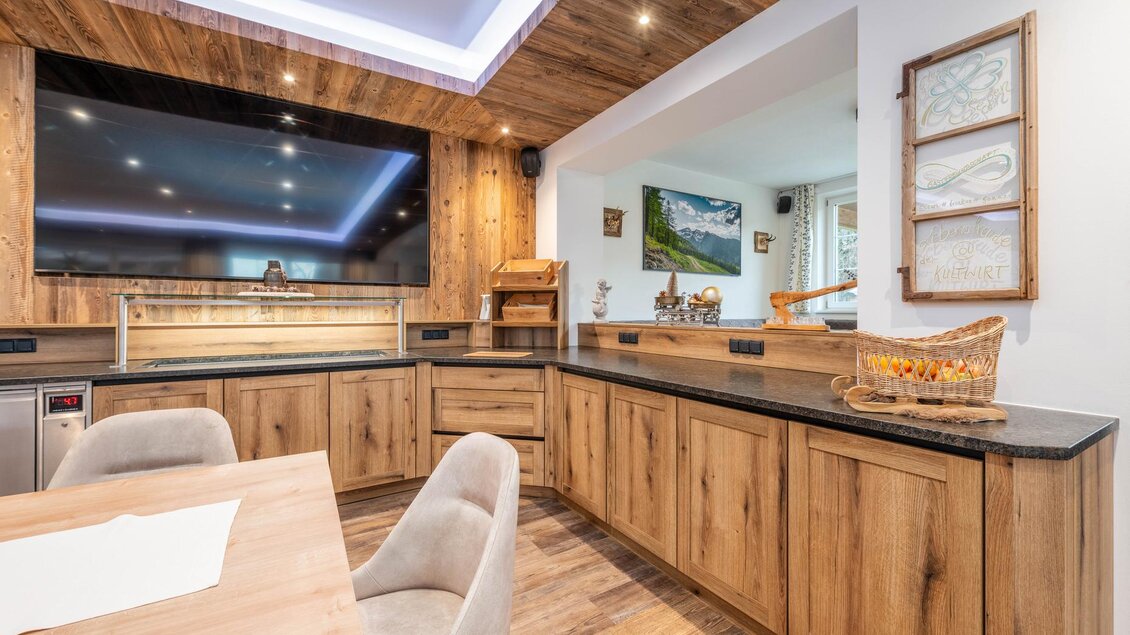 Eine moderne Küche mit Holzdesign und eleganten Details. Der Raum ist hell und einladend, ausgestattet mit einem großen Fernseher und stilvollen Dekorationen.